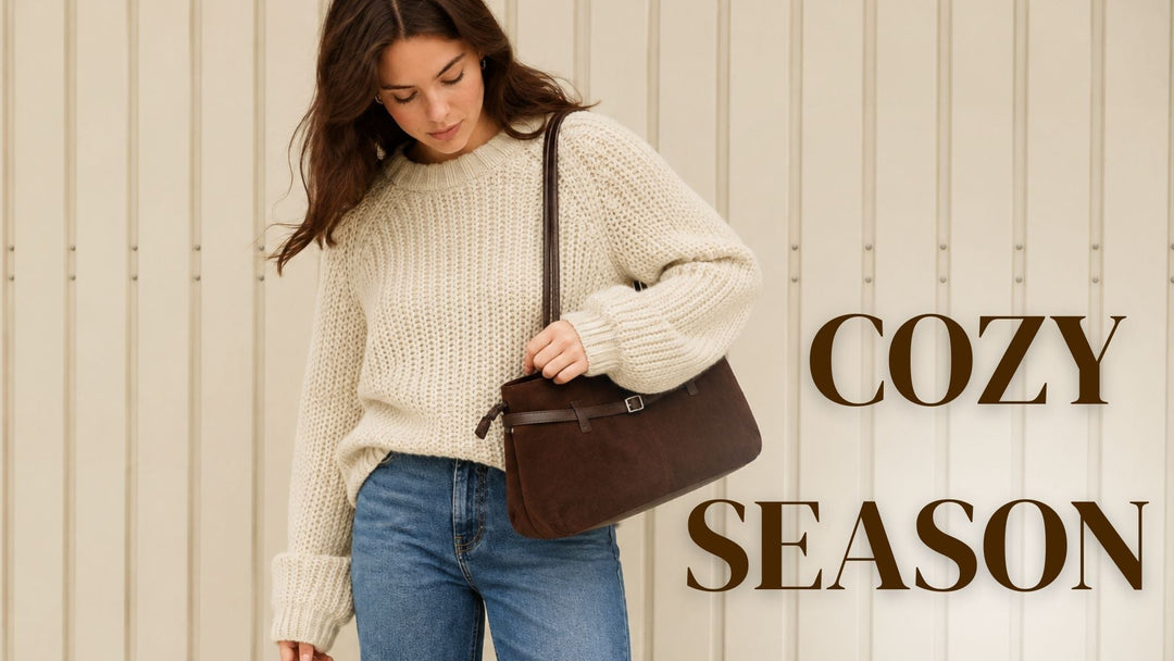 Junge Frau mit schokobraunen Haaren trägt einen beigen Grobstrickpullover, eine dunkelblaue Wide-Leg-Jeans und eine braune Wildleder-Schultertasche vor einer hellen Wand. Rechts steht der Schriftzug „COZY SEASON“ in großen braunen Buchstaben.