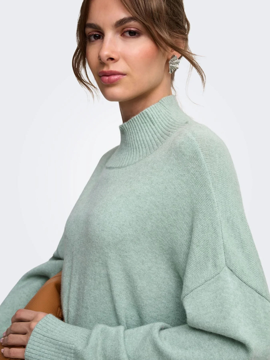 Cremeweißer Strickpullover mit feinem Ajourmuster, kombiniert mit einer schwarzen Hose, vor hellem Studiohintergrund.