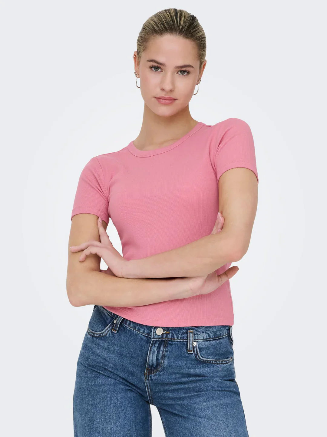 Blondhaarige Frau, Harre zu strengen Zopf zusammengebunden pinkes T-Shirt an und enge blaue Jeanshose.