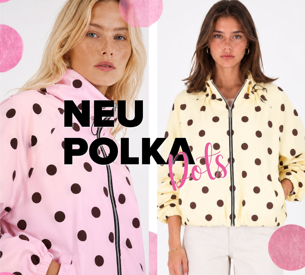 Banner mit zwei weiblichen Models in Jacken mit großem Polka-Dot-Muster. Links trägt das Model eine rosafarbene Jacke mit dunkelbraunen Punkten, rechts eine cremegelbe Variante mit demselben Muster. Beide Jacken haben einen Reißverschluss und einen elastischen Saum. Im Mittelpunkt steht der Schriftzug „NEU POLKA Dots“, ergänzt durch dekorative rosa Punkte auf hellem Hintergrund.